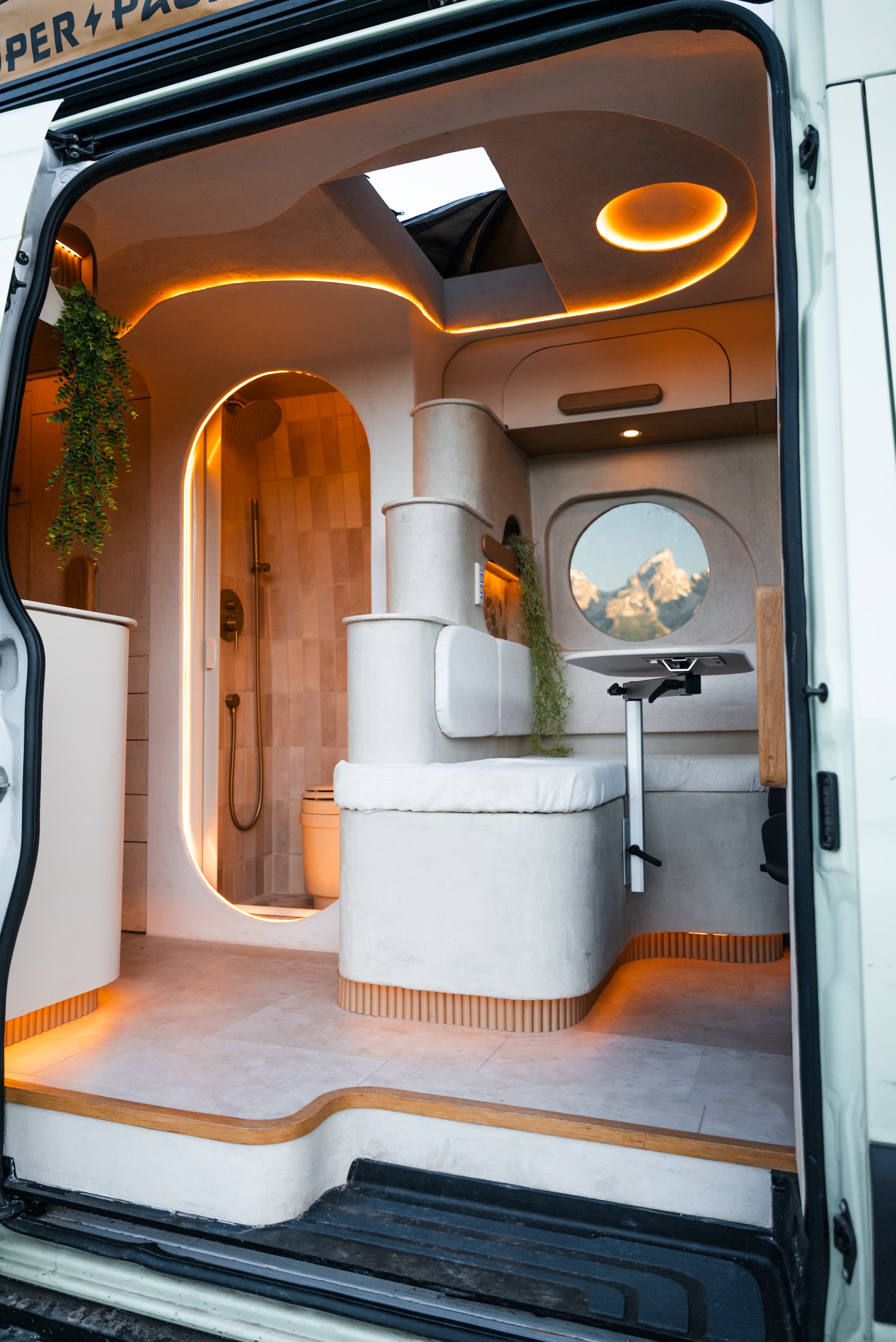Inside the Flow: a sculpted plaster interior with warm cove lighting, an arched tiled shower, and a porthole window framing the mountains.